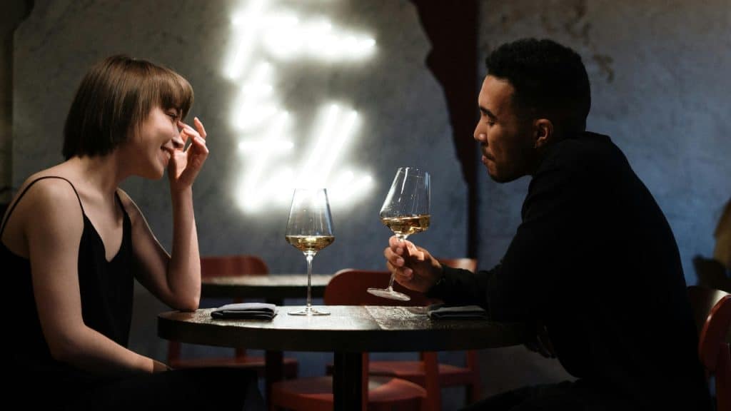 A woman laughing while sitting at a table across from a man holding wine.