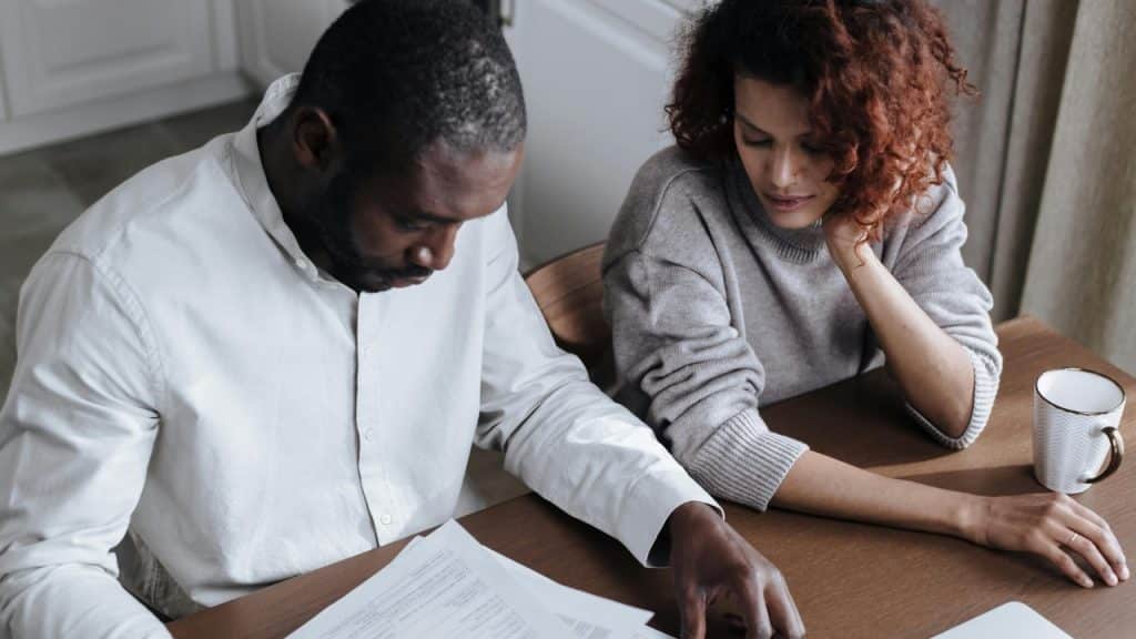 A man and woman sit at a wooden table looking over documents together.