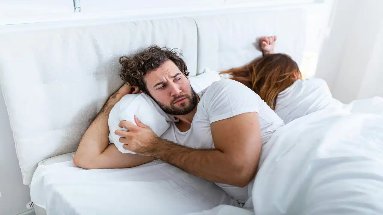 A man looking bothered while his wife sleeps