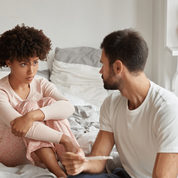 Unhappy couple sitting on bed looking at each other