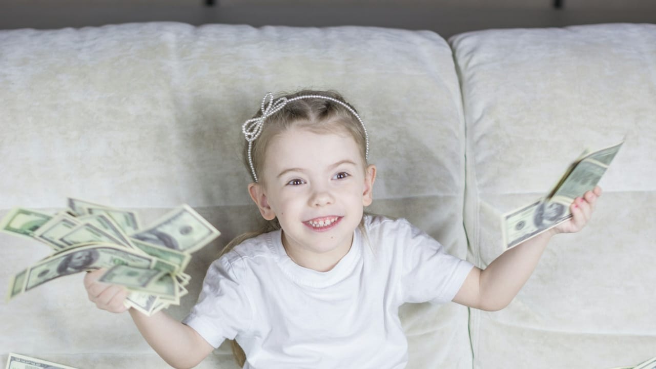 A little girl sitting on a couch holding money.