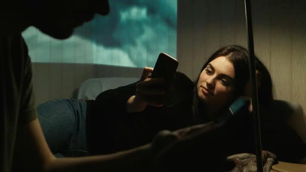 A woman lying down and looking at her phone in dim lighting.