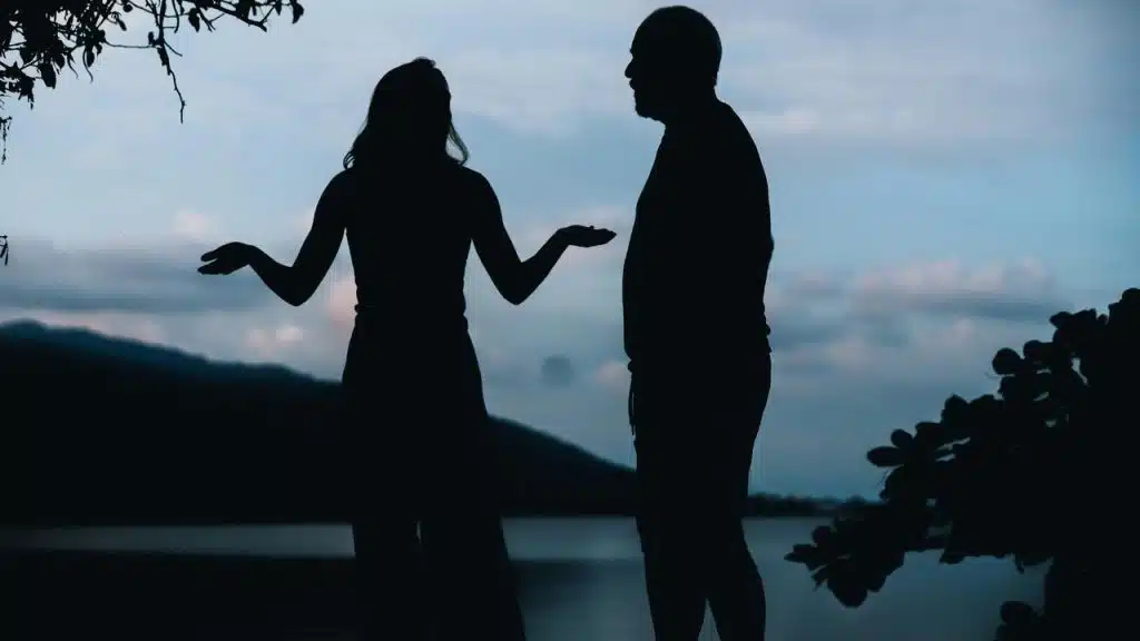 A silhouetted couple standing and talking by the water.