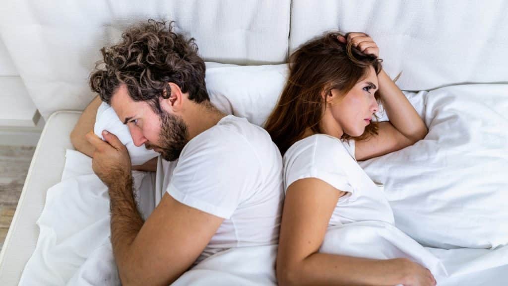A man and a woman lie in bed facing away from each other.
