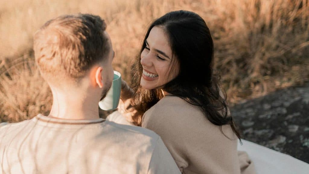 A couple sits outdoors, smiling at each other