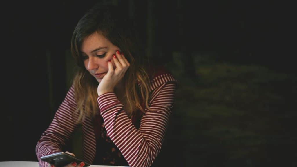 A woman looking down at her phone with her head resting on her hand.