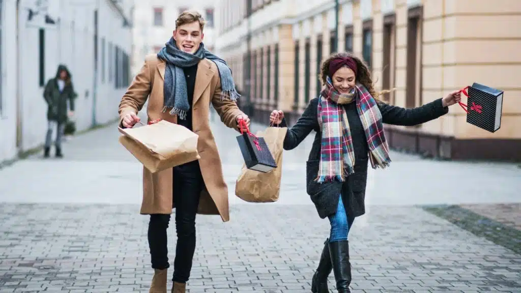 A man and woman walk down a street carrying several shopping bags and smiling broadly.