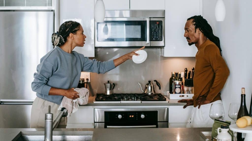 A woman in a kitchen points a small white plate toward a man standing near her.