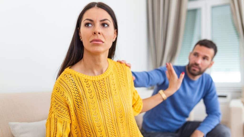 A woman in a yellow sweater holds up a hand while a man reaches out.