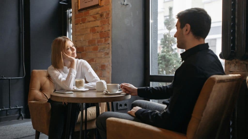 A woman in a white shirt and a man in black sit at a cafe.