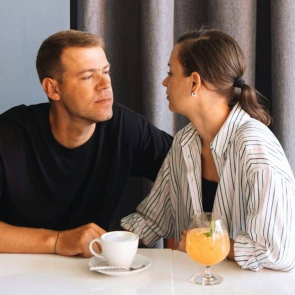 A man and a woman sit at a table looking at each other indoors.
