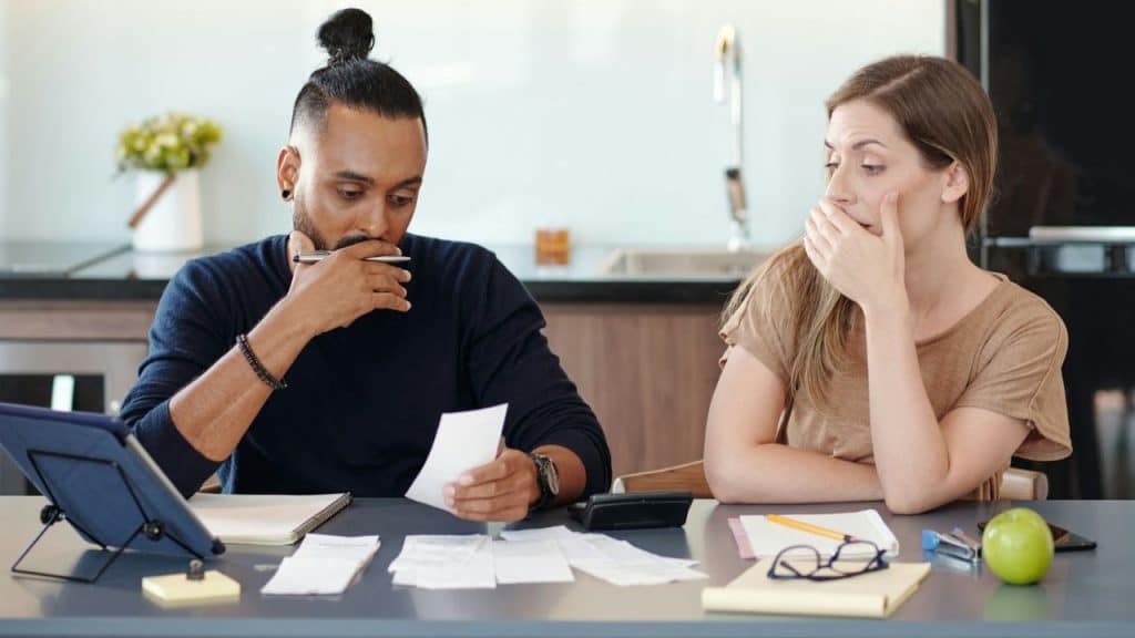 A man and woman sit at a table reviewing several receipts and financial documents together.
