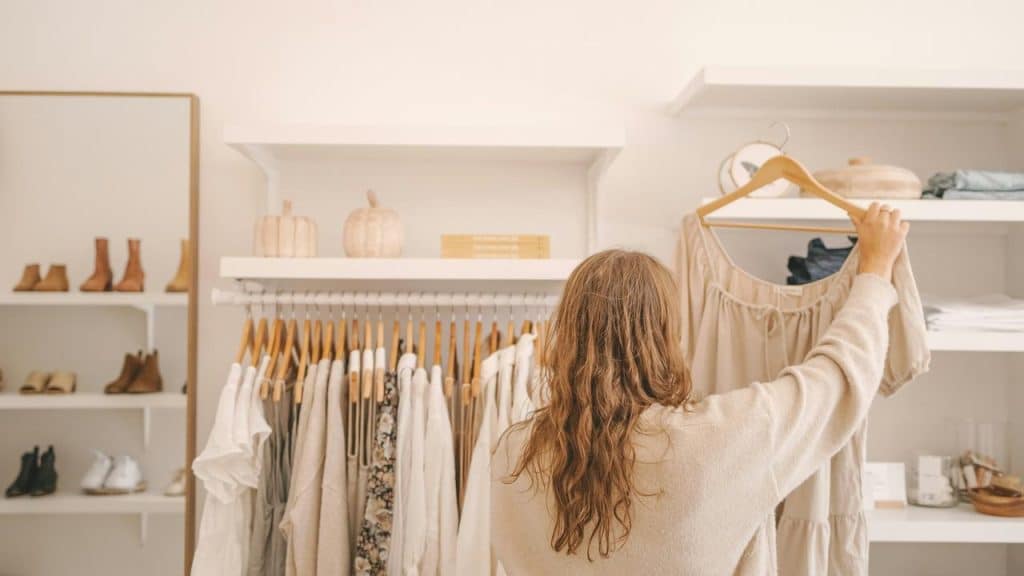 A woman browsing clothes and holding a dress on a hanger in a boutique