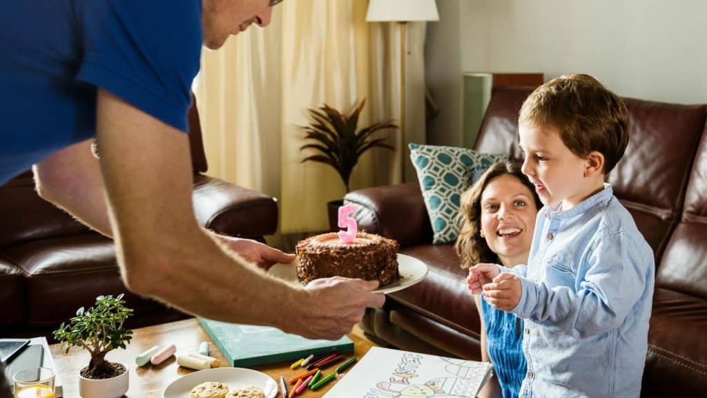 A man presents a birthday cake with a number five candle to a young child.