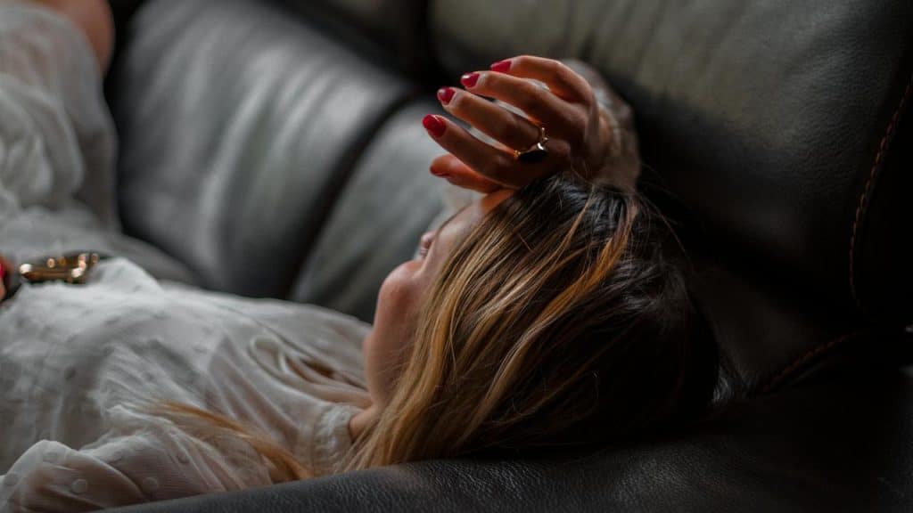 A person lying on a couch with an arm raised near their face.