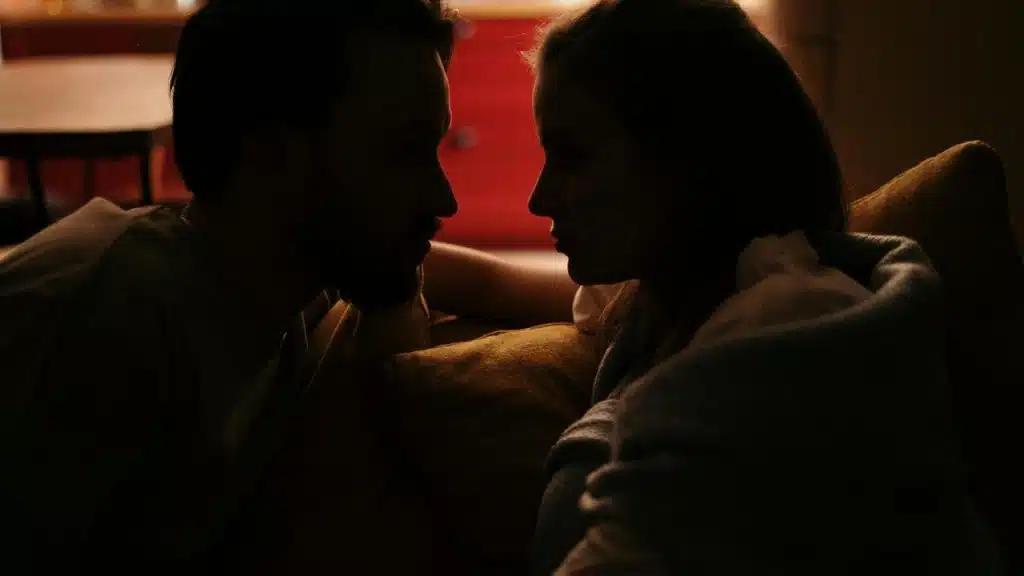 A couple sitting close together in dim light, facing each other.