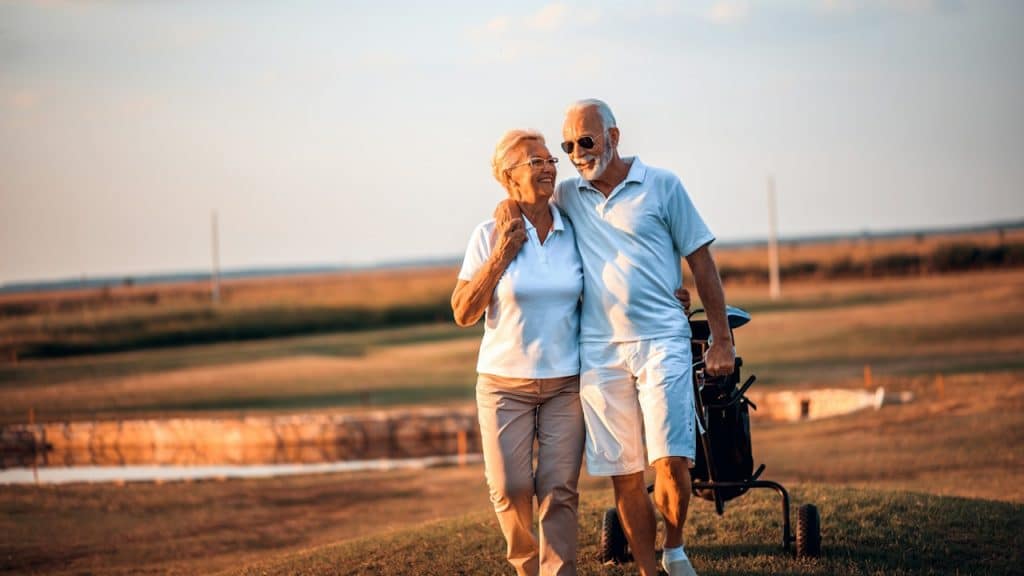 A mature couple on a golf course with the man placing his arm around his wife’s shoulder.