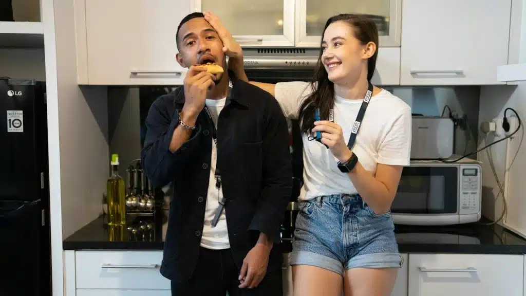 A man and a woman eating food in a kitchen.