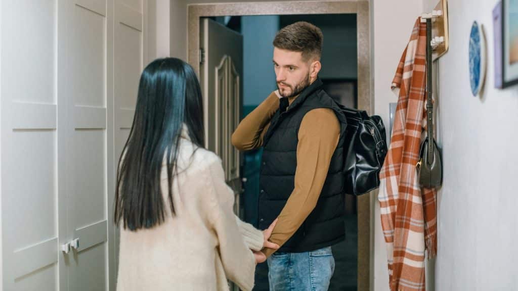 A man with a black bag stands in a doorway looking back at a woman's arm.