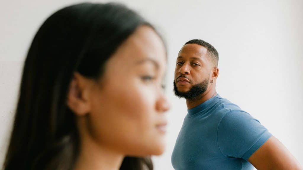 A blurred woman is in the foreground, while a man in a blue shirt looks over her shoulder.