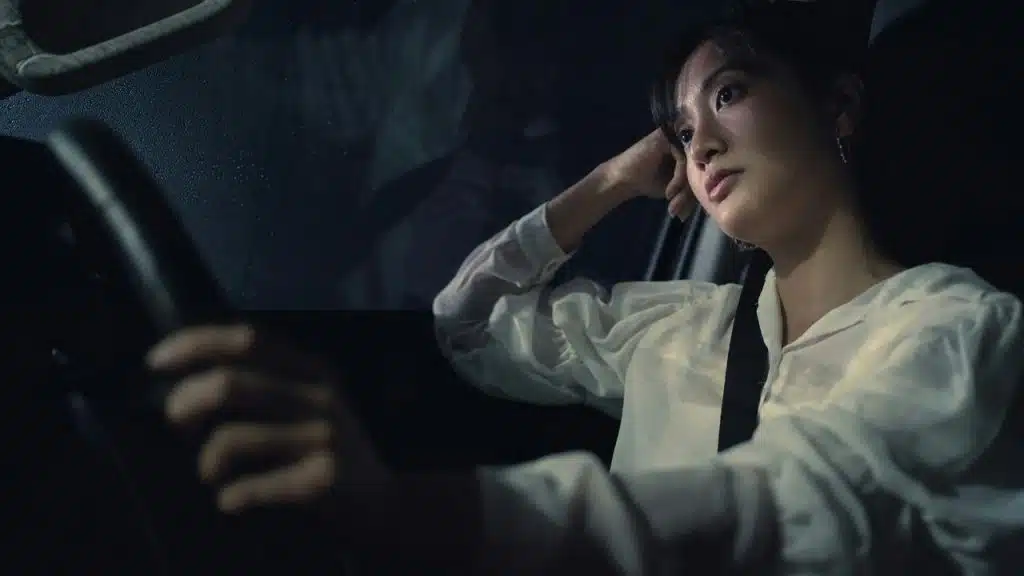 A woman driving a car at night with a thoughtful expression.