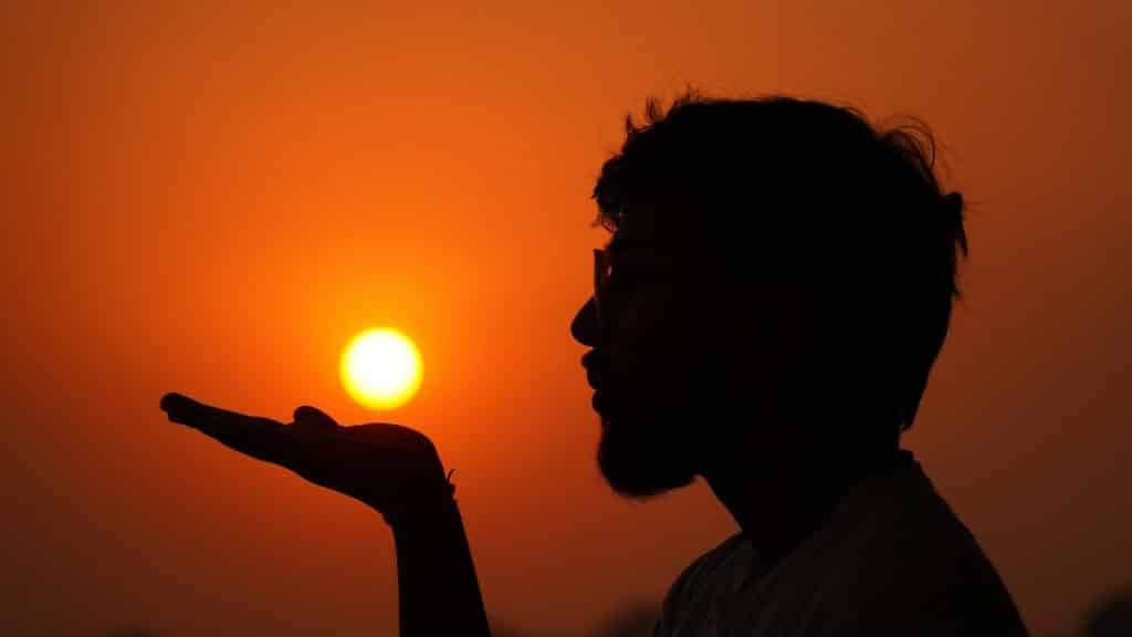 A silhouette of a man holding his hand out to the sun.