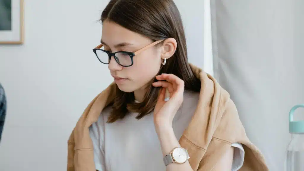 A woman wearing glasses looking down thoughtfully.