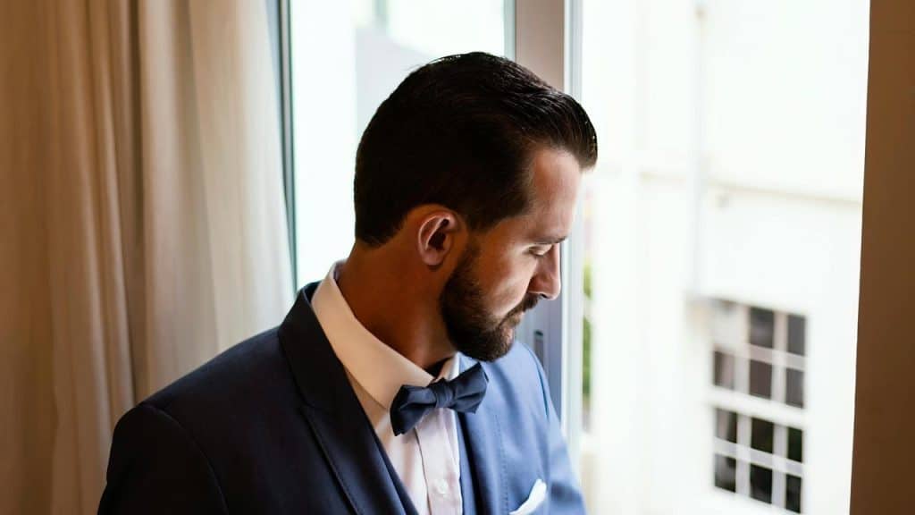A man in a suit and bow tie looking out a window.