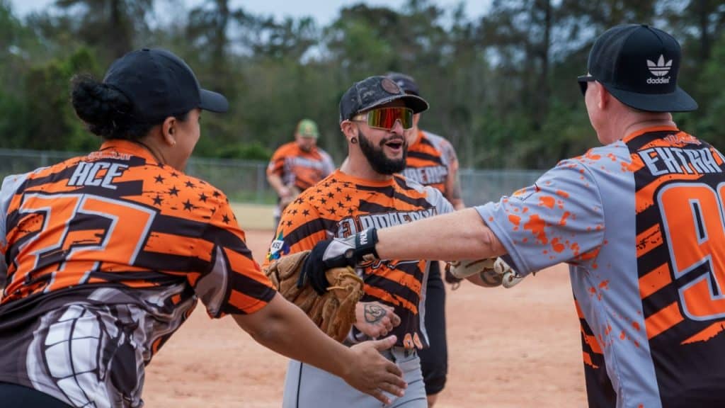 Three baseball players in orange and black jerseys celebrate with a high-five.