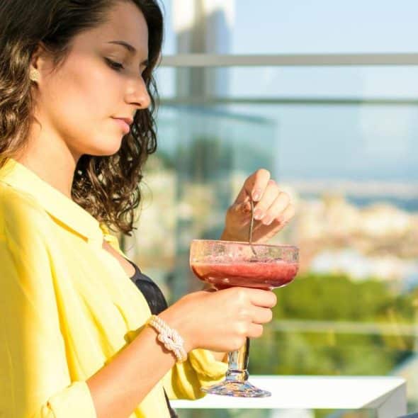 A woman holding a drink while relaxing on a balcony.