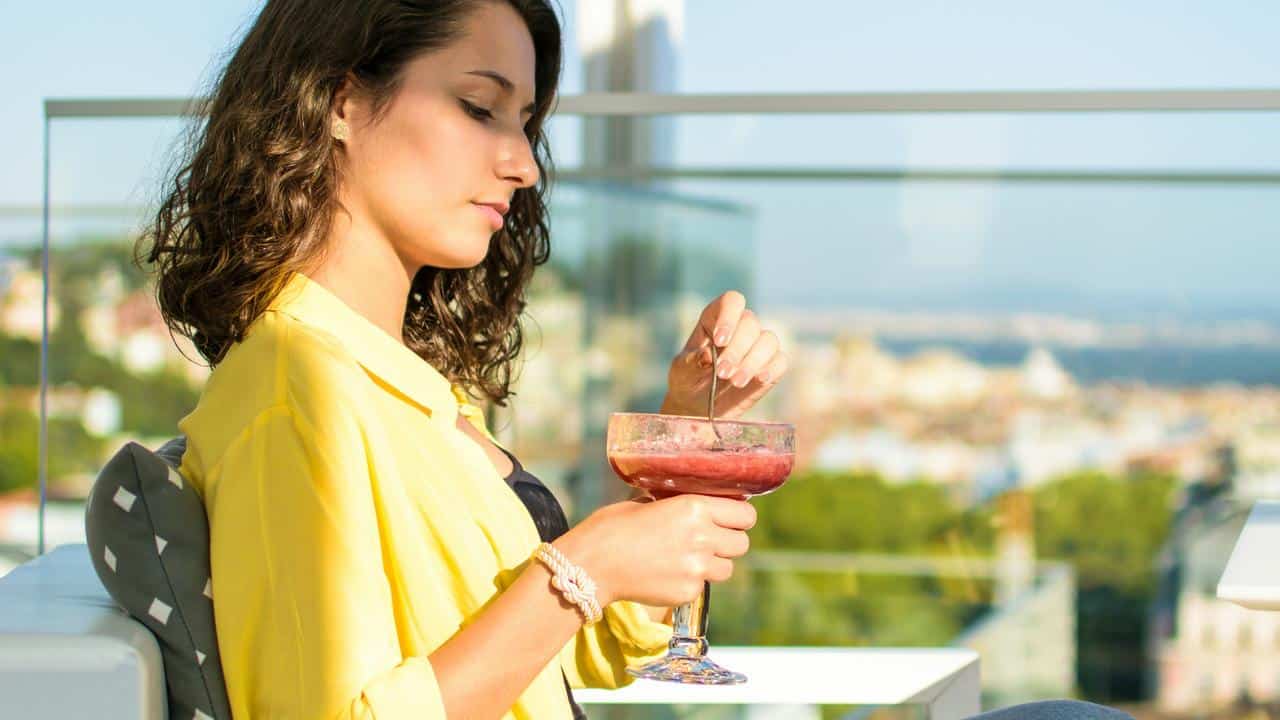 A woman holding a drink while relaxing on a balcony.