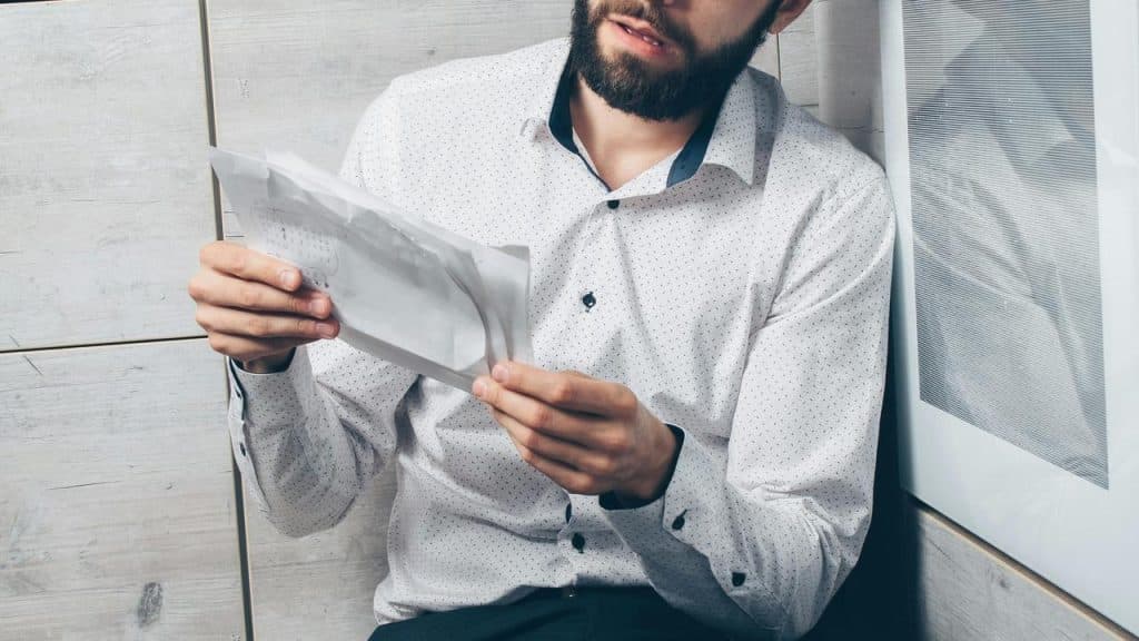 A man sitting on the floor reading a letter with a concerned expression.