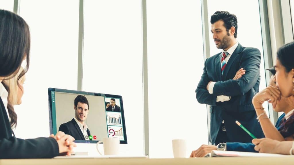 A group of professionals in an office meeting with someone via video call.