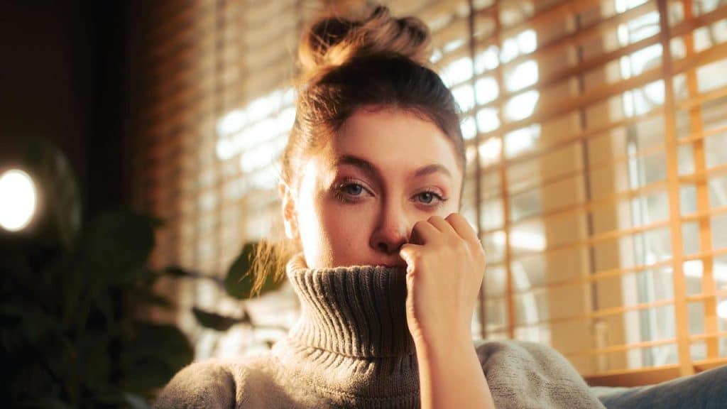 A woman looking thoughtful while sitting by a window.