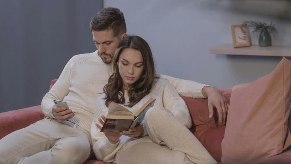 A man looks at his phone while a woman sits next to him reading.