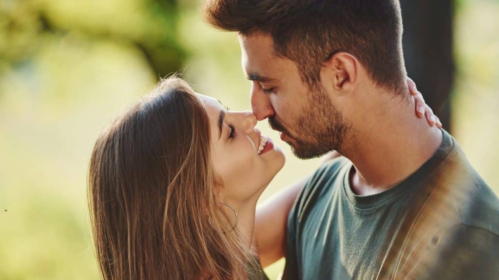 A close-up profile view of a man and woman leaning in toward each other outdoors.