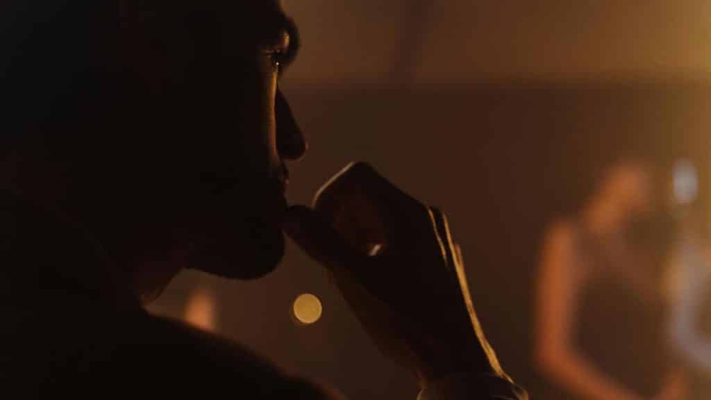 A man in dim light resting his hand near his mouth.