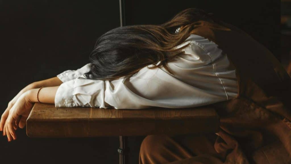 A woman resting her head on a table with her arms outstretched.