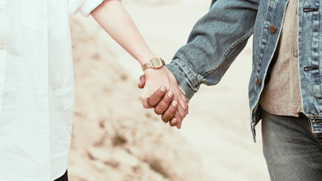 A close-up view of two people holding hands, one wearing a gold watch.