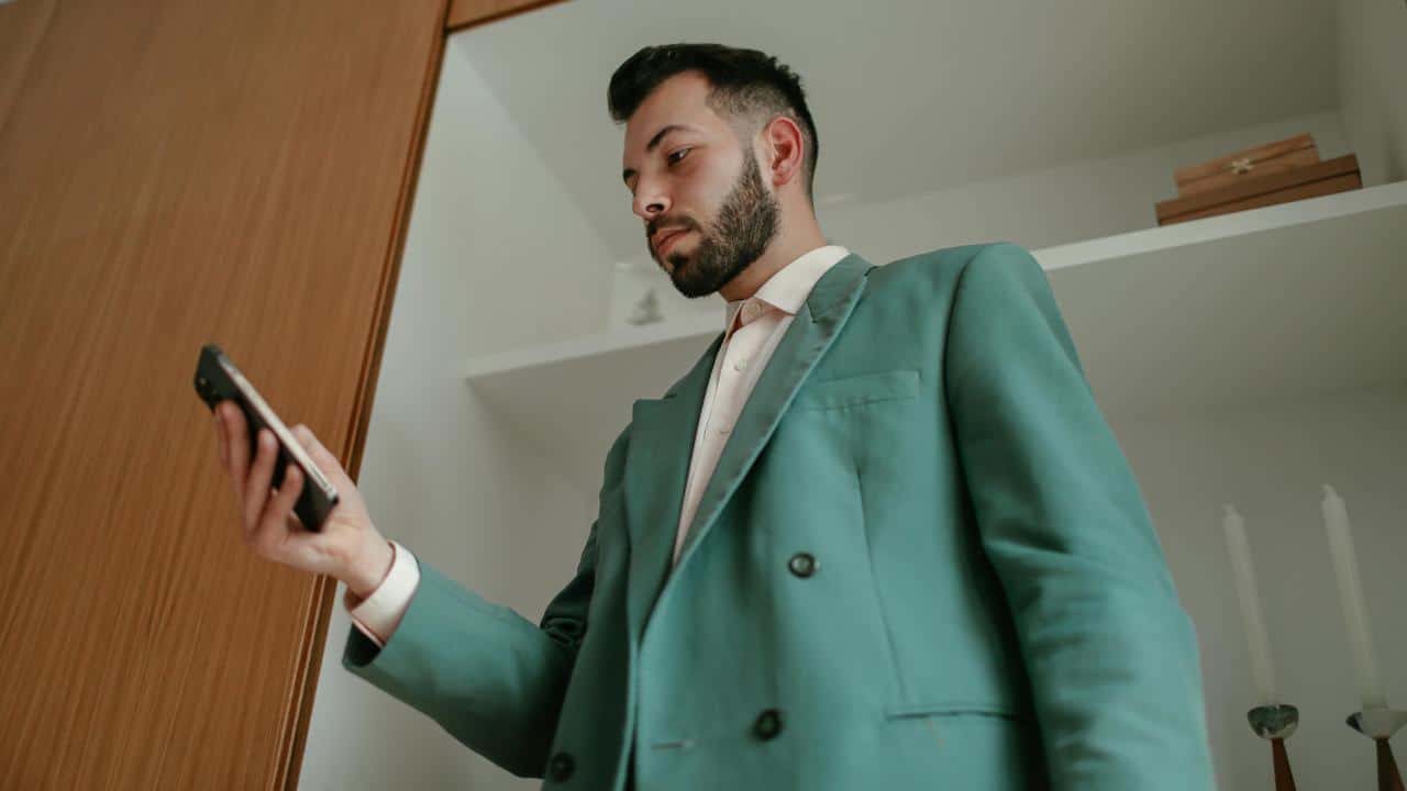 A man in a teal suit looks at his phone