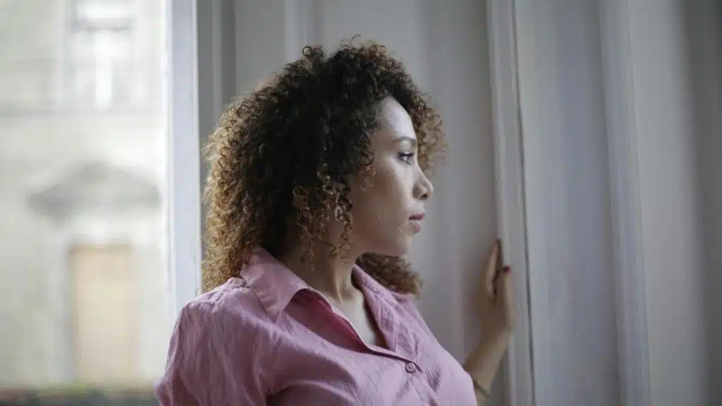 A woman in a pink shirt looking out of a window