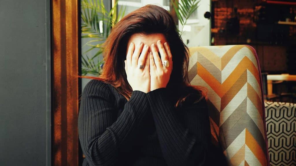 A woman sitting with her face covered by her hands.