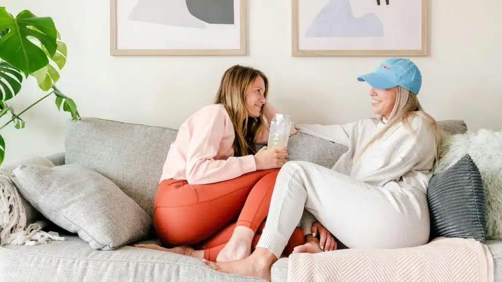 A woman sitting on a couch talking and smiling with another woman.