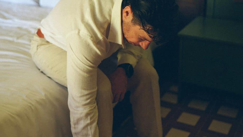 A man sitting on a bed with his head lowered.