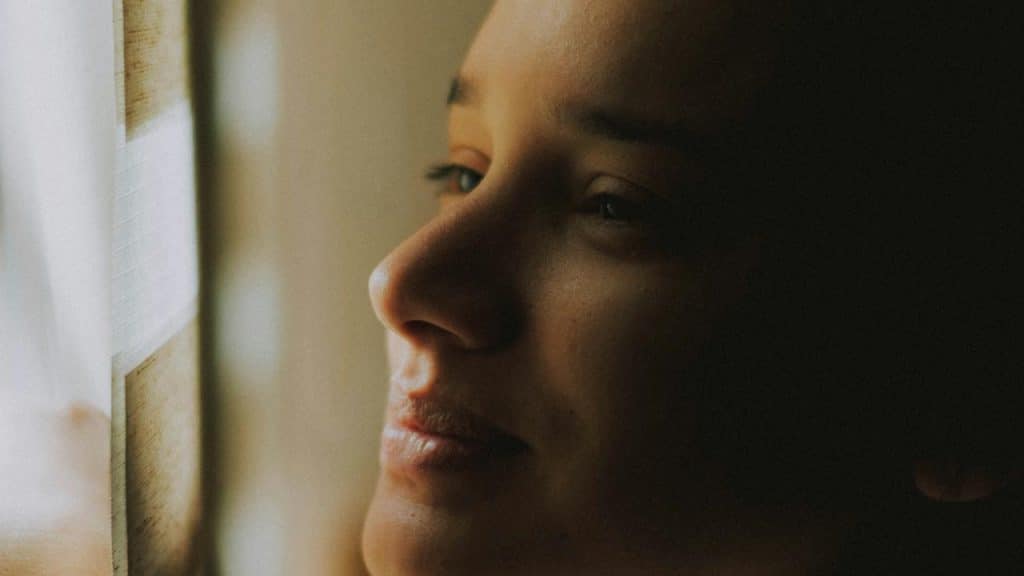 A person gazing out a window with a soft expression.