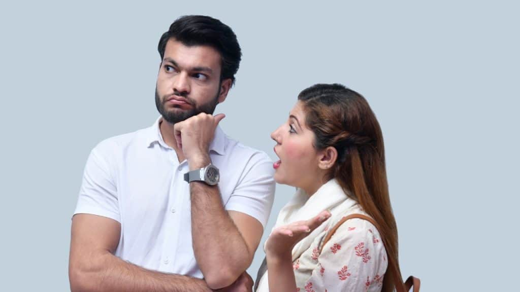 A man rests his chin on his hand while a woman gestures toward him.