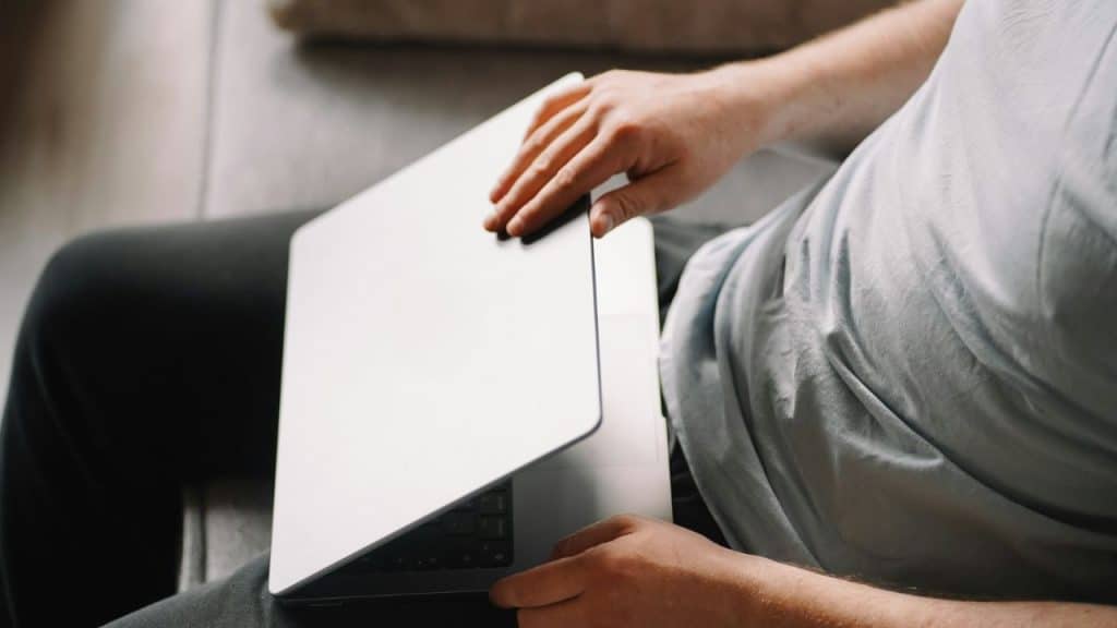 A top-down view of a person’s hands closing a silver laptop lid on their lap.