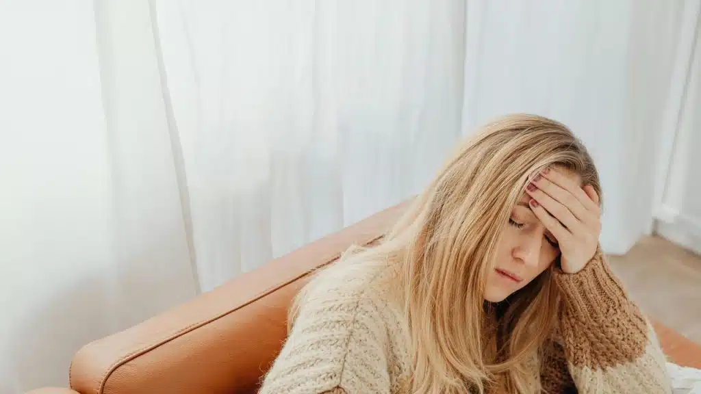 A woman sitting on a couch with her hand on her forehead.