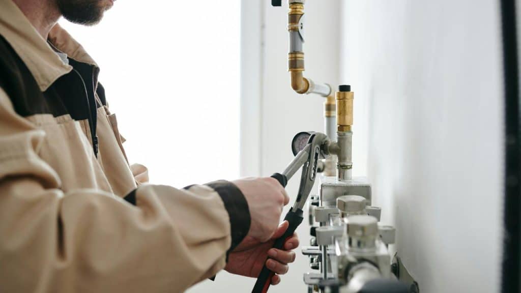 A person using a wrench to adjust pipes and a pressure gauge on a wall.