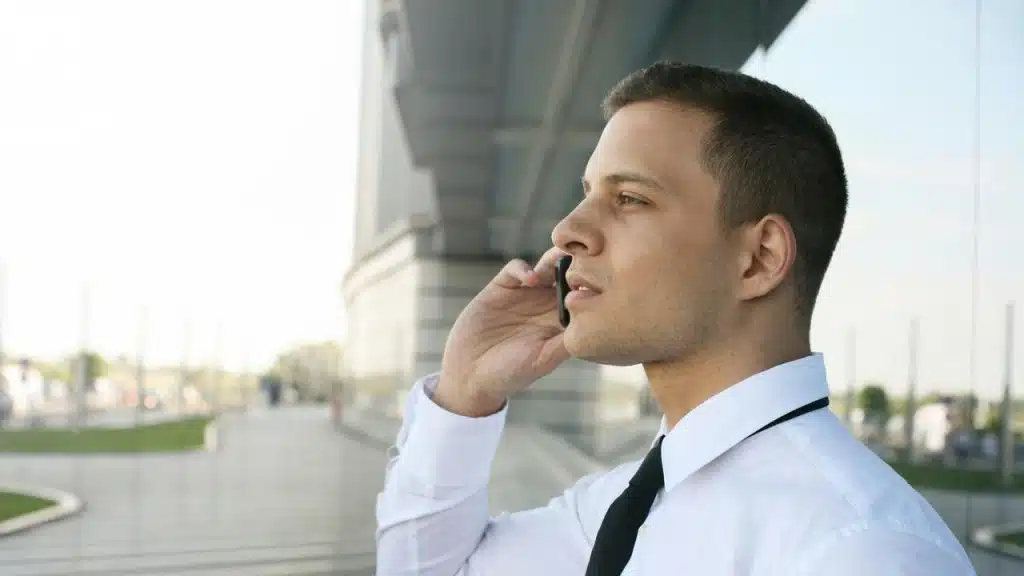 A man in a dress shirt talking on a phone while standing outdoors.